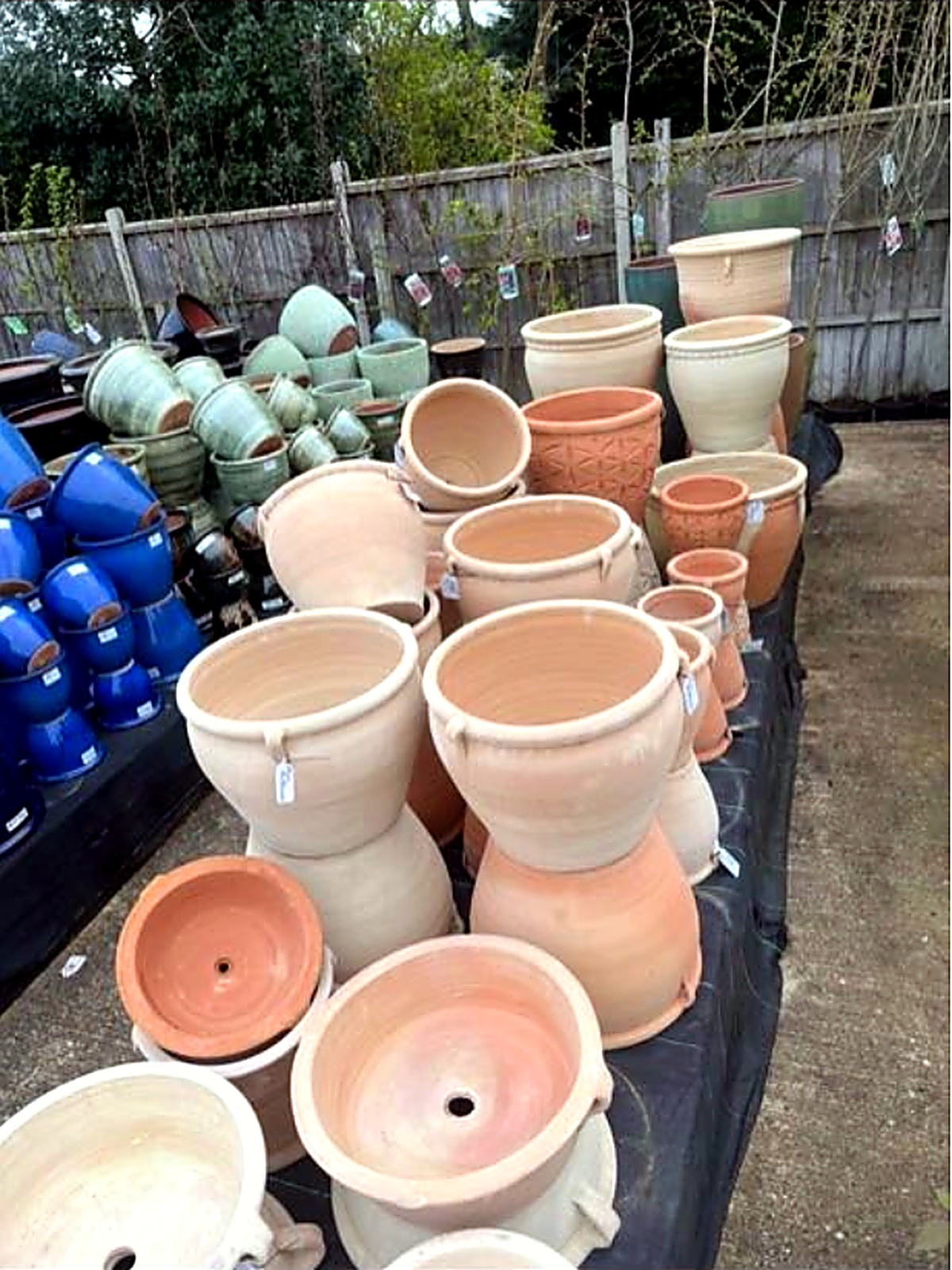 Terracotta and green glazed pots arranged outdoors along the fence