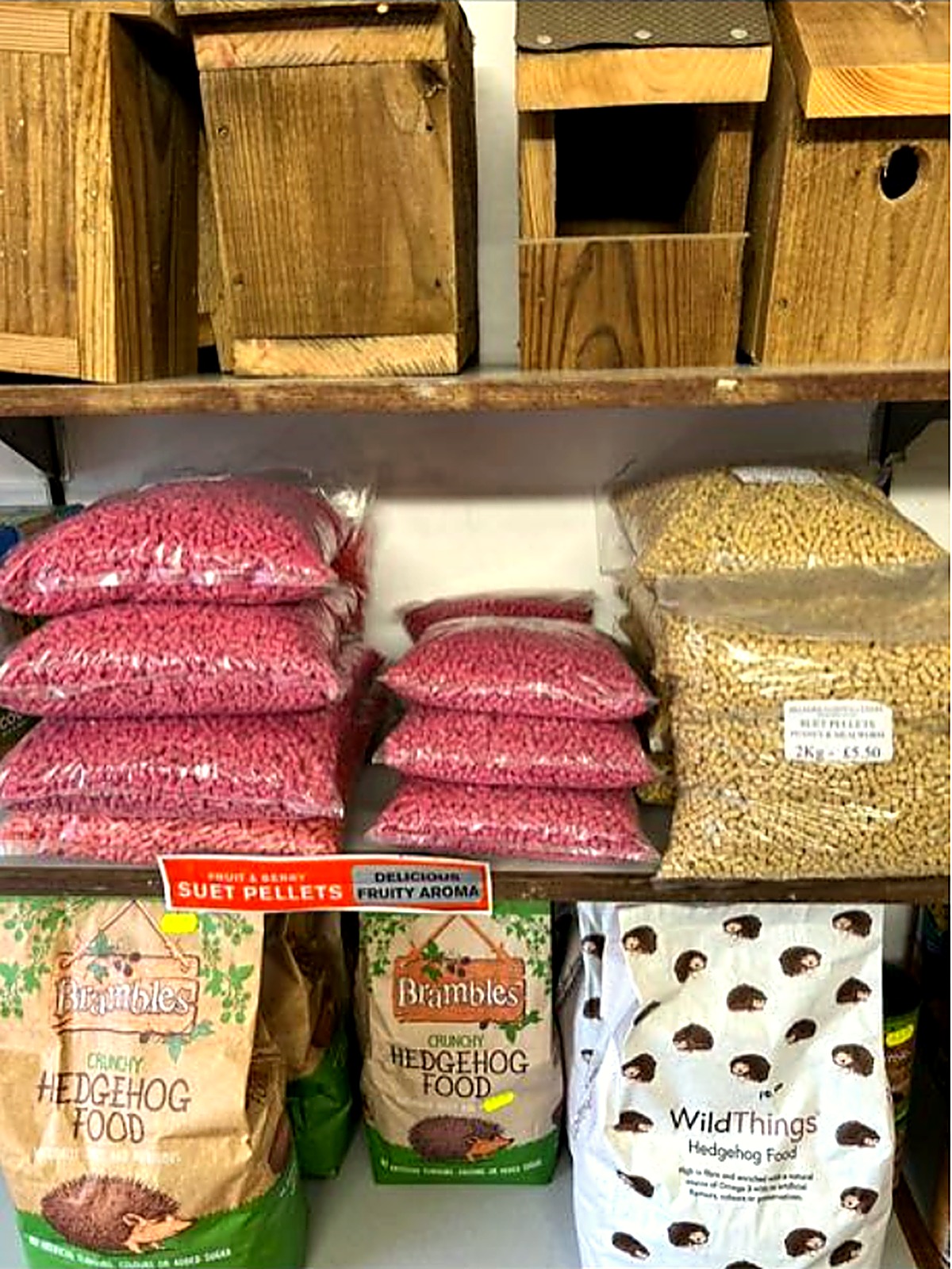 Wooden bird boxes above suet pellets and hedgehog food on the shelves